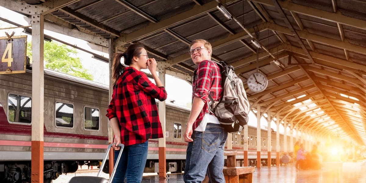 Dos amigos con mochilas charlando en el andén de una estación